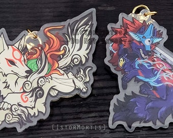 May include: Two clear acrylic keychains featuring anime-style wolf characters. The first keychain depicts a white wolf with red and gold accents, while the second keychain features a blue and black wolf with red accents. Both keychains have a gold metal ring.