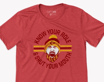 May include: Red t-shirt featuring a graphic of a football player's face within a circle. The text surrounding the face reads "Know Your Role & Shut Your Mouth".