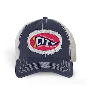 May include: A navy blue and white trucker hat with a distressed red oval patch that says "St. Louis Soccer City 2023 Inaugural Season".