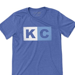 May include: A blue t-shirt with a white and blue "KC" graphic printed on the front.