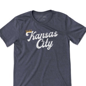 Puede incluir: Una camiseta azul marino con un gr&aacute;fico blanco que dice "Kansas City" con una corona dorada sobre la palabra "Kansas".