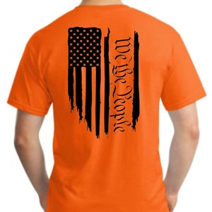 Puede incluir: Camiseta naranja con una bandera estadounidense negra desgastada y el texto "We the People" impreso en la espalda.