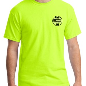 Puede incluir: Una camiseta amarilla brillante con un parche circular negro en el pecho izquierdo. El parche tiene una bandera estadounidense en blanco y negro y el texto "PATRIOT HI VIS".