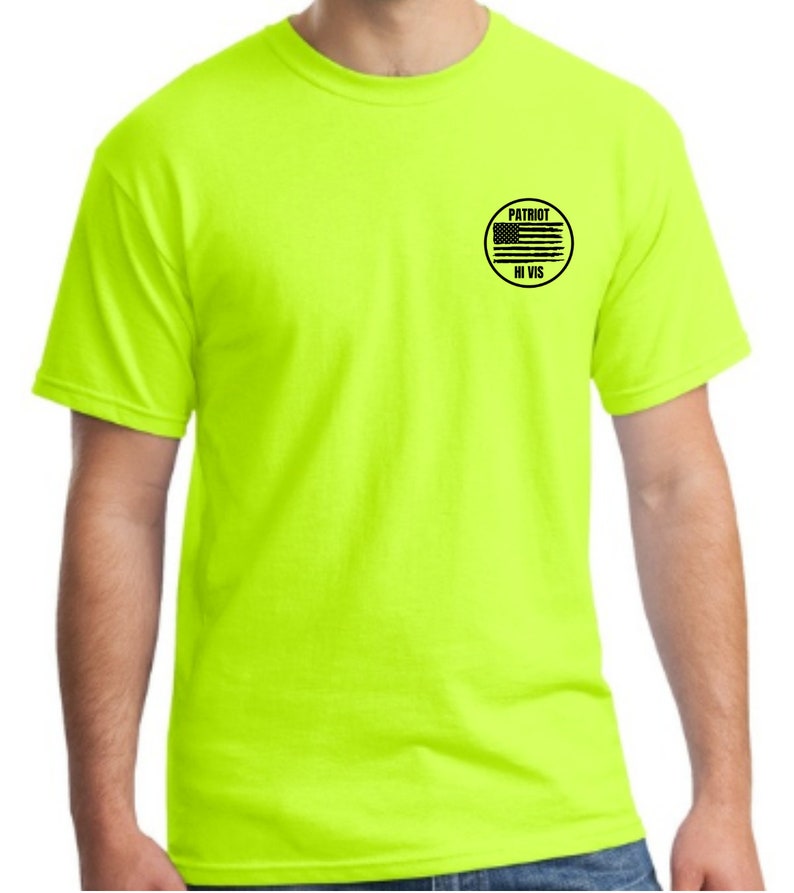 Puede incluir: Una camiseta amarilla brillante con un parche circular negro en el pecho izquierdo. El parche tiene una bandera estadounidense en blanco y negro y el texto "PATRIOT HI VIS".