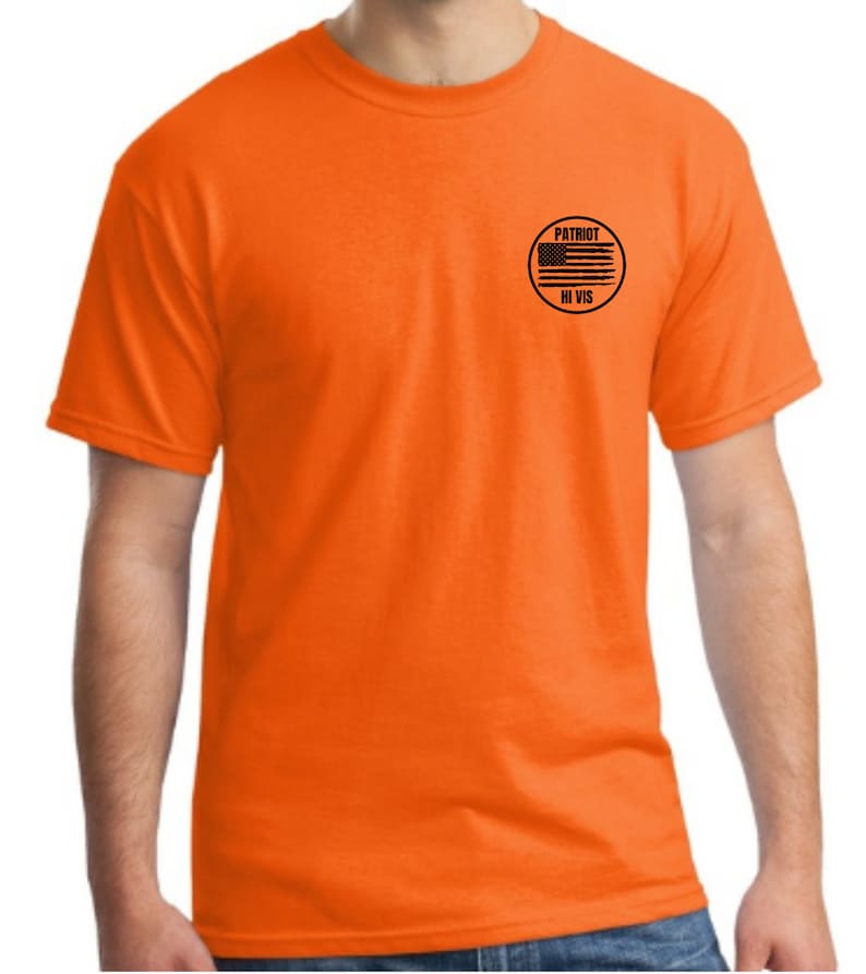 Puede incluir: Camiseta naranja de manga corta con un parche circular negro en el pecho izquierdo. El parche tiene una bandera estadounidense en blanco y negro y el texto "PATRIOT HI VIS".