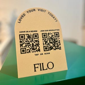 Peut inclure: Un panneau beige avec des bords supérieurs arrondis. Il comporte deux codes QR, le texte "LEAVE US A REVIEW", "JOIN OUR NEWSLETTER", "TAP OR SCAN" et "FILO". Le panneau indique "LOVED YOUR VISIT TODAY?" dans une police incurvée.