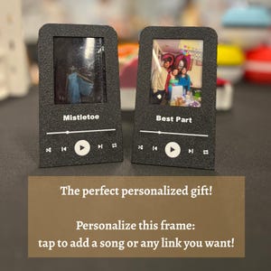 May include: Two black photo frames shaped like music players, each displaying a photo. One says "Mistletoe," the other "Best Part." White text on the frames includes play, skip, and rewind symbols. A brown sign below reads "The perfect personalized gift!"