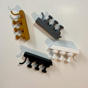 Può includere: Quattro mini portabicchieri da vino stampati in 3D in vari colori: giallo senape, grigio, nero e bianco. Ogni portabicchieri può contenere tre bicchieri e ha un manico curvo per appenderlo. I portabicchieri sono progettati per piccoli calici da vino.