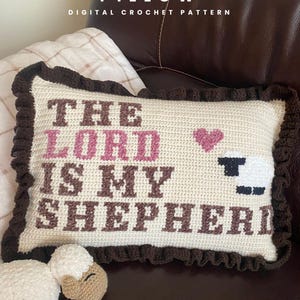 May include: A rectangular crochet pillow with a cream-colored base, featuring the brown and pink text "THE LORD IS MY SHEPHERD" and a small pink heart and white sheep graphic. The pillow has a dark brown ruffled border and includes the text "@SHIIMADE".