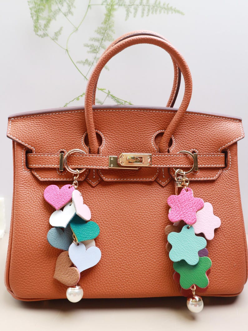 May include: A brown leather handbag with gold hardware and two charms. One charm is a cluster of colorful hearts and the other is a cluster of colorful stars.