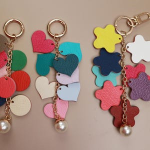 May include: Three colorful keychains with different shapes and colors. Each keychain has a gold chain and a pearl charm. The keychains feature hearts, stars, and circles in various colors, including pink, blue, green, red, and purple.