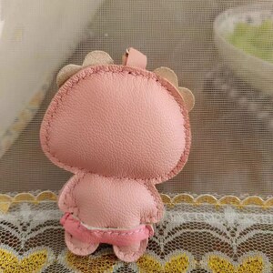May include: A pink leather keychain shaped like a cartoon character with a stitched face and a small loop for attaching keys.