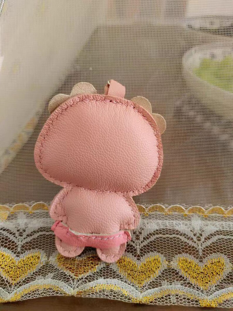 May include: A pink leather keychain shaped like a cartoon character with a stitched face and a small loop for attaching keys.