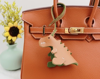 May include: A brown leather handbag with a gold clasp and a green and brown dinosaur key charm.