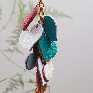 May include: A gold chain keychain with a pearl charm and multiple leather heart charms in shades of pink, blue, and white.