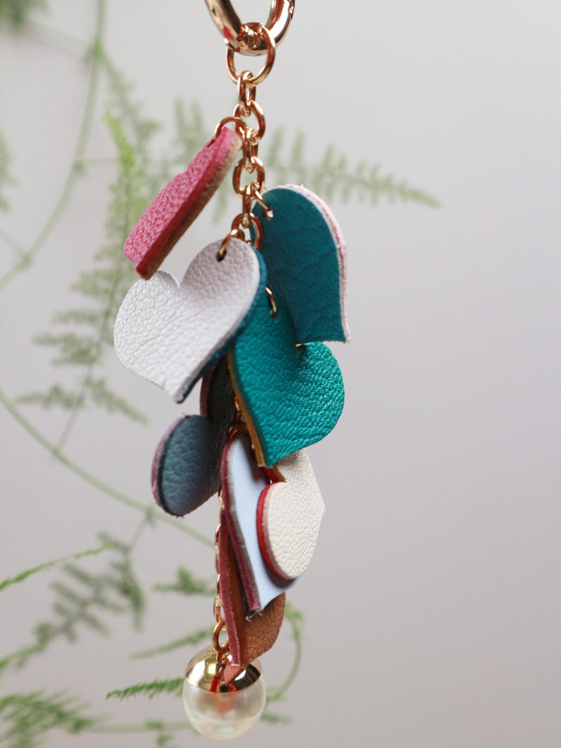 May include: A gold chain keychain with a pearl charm and multiple leather heart charms in shades of pink, blue, and white.