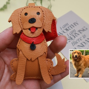 May include: A handcrafted leather dog keychain in a sitting position. The dog has a tan body, black nose, and red collar. The keychain is a charming accessory for dog lovers.
