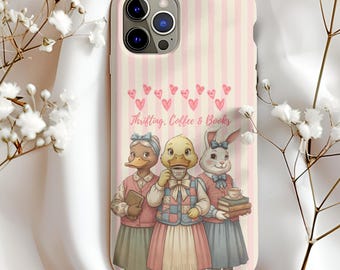 Könnte beinhalten: Handyhülle mit rosa und weißen Streifen, die drei anthropomorphe Tierfiguren zeigt: eine Ente, ein Entlein und ein Kaninchen. Der Text "Thrifting, Coffee & Books" steht über den Figuren, mit rosa Herzen.