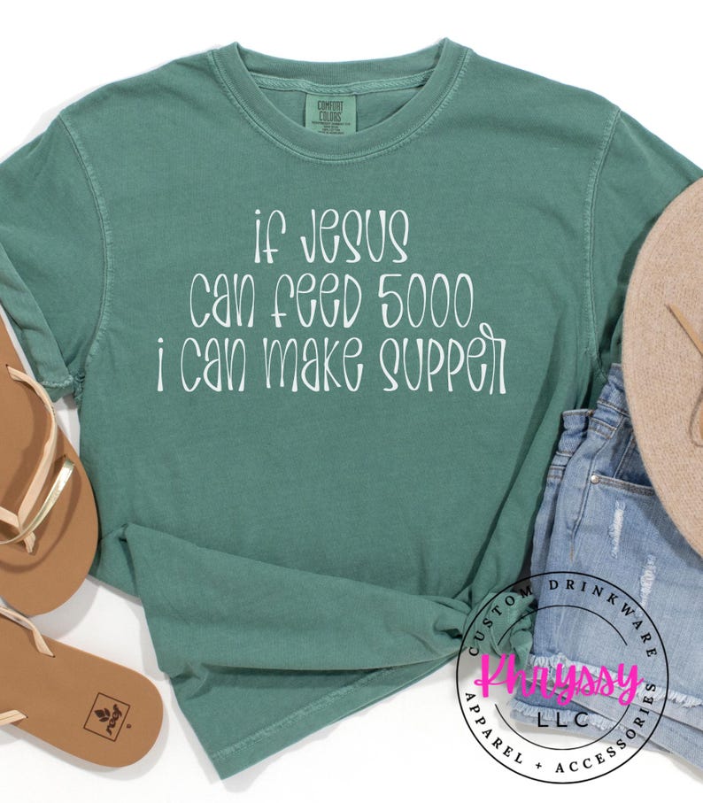 May include: A teal long-sleeve shirt with the text "if Jesus can feed 5000, I can make supper" in white script. The shirt is knotted at the waist. Accessories include sandals and a hat.