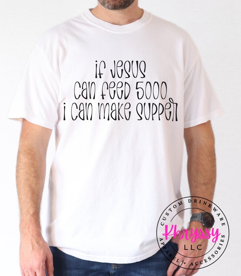 May include: White t-shirt with the text "If Jesus can feed 5000, I can make supper" in black script. The shirt is a casual style, suitable for everyday wear. The shirt also has a logo on the bottom right.