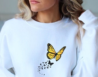May include: White sweatshirt with a yellow butterfly graphic. The butterfly is flying away from a trail of smaller butterflies.