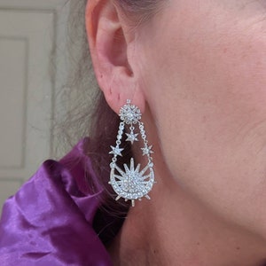 May include: Silver dangle earrings with a crescent moon and sun design, adorned with sparkling clear crystals.