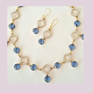 May include: A gold necklace and earring set. The necklace and earrings feature square frames with small white beads, connected by gold links. Each piece has blue, square gemstones. The earrings have gold hooks.