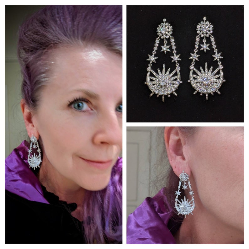 May include: A pair of silver dangle earrings with a crescent moon and sun design. The earrings are adorned with clear crystals and have a starburst pattern.