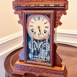 May include: Antique wooden clock with a carved frame and a glass face. The clock face has Roman numerals and a black and white design.
