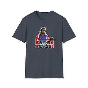 Könnte beinhalten: Ein marineblaues T-Shirt mit einem Aufdruck von Andre Agassi in einem farbenfrohen Tennisoutfit, der einen Tennisschläger hält. Der Text "Andre the Agassi" ist in roten, blauen und weißen Buchstaben gedruckt.