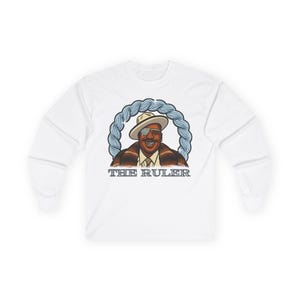 May include: White long-sleeve shirt featuring a cartoon illustration of a man wearing a hat and sunglasses, with the text "THE RULER" below the image. The illustration is surrounded by a blue rope design.