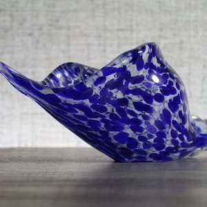 May include: A blue and white glass bowl with a speckled pattern. The bowl is shaped like a seashell and has a wavy edge.