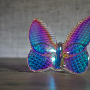 K&ouml;nnte beinhalten: Eine Schmetterlingsfigur aus irisierendem Glas mit einer texturierten Oberfl&auml;che im Rautenmuster, die lebhafte Violett-, Blau- und T&uuml;rkist&ouml;ne reflektiert. Die Fl&uuml;gel sind durchscheinend mit einer gl&auml;nzenden Oberfl&auml;che und einem Mittelk&ouml;rper.