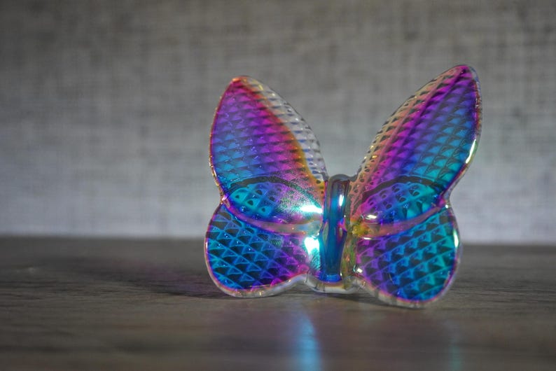 K&ouml;nnte beinhalten: Eine Schmetterlingsfigur aus irisierendem Glas mit einer texturierten Oberfl&auml;che im Rautenmuster, die lebhafte Violett-, Blau- und T&uuml;rkist&ouml;ne reflektiert. Die Fl&uuml;gel sind durchscheinend mit einer gl&auml;nzenden Oberfl&auml;che und einem Mittelk&ouml;rper.