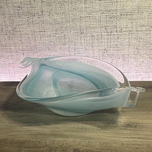 May include: A clear glass bowl featuring swirling patterns of light blue and white. The bowl has an elongated, organic shape with pointed ends and curved, undulating edges that create a fluid, wave-like appearance throughout the glass.