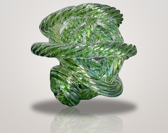 May include: A translucent green glass sculpture featuring a complex, knotted design of intertwined, spiraled glass rods. The object has a glossy, reflective surface with varying shades of light and dark green, creating a sense of depth.