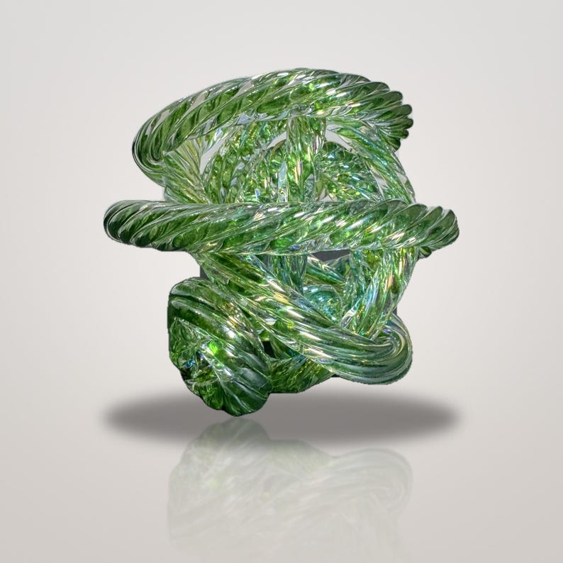 May include: A translucent green glass sculpture featuring a complex, knotted design of intertwined, spiraled glass rods. The object has a glossy, reflective surface with varying shades of light and dark green, creating a sense of depth.