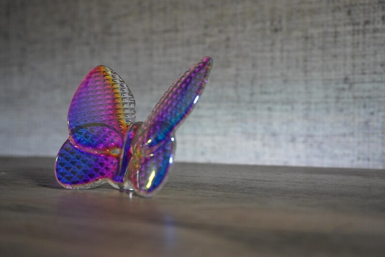 K&ouml;nnte beinhalten: Eine durchscheinende Schmetterlingsfigur mit einer lebendigen, irisierenden Oberfl&auml;che, die zwischen Violett-, Blau- und Oranget&ouml;nen wechselt. Die Fl&uuml;geloberfl&auml;che weist ein markantes, rautenf&ouml;rmiges Gittermuster auf, das das Licht reflektiert.