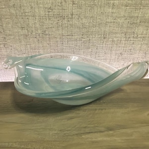 May include: A decorative glass bowl featuring a fluid, elongated leaf-like shape with swirling patterns of translucent light blue and white colors. The bowl has smooth, curved edges and a polished finish, creating a soft, layered appearance.