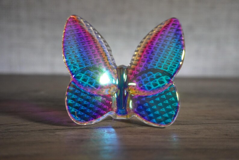 K&ouml;nnte beinhalten: Eine durchscheinende Schmetterlingsfigur mit einer lebendigen, irisierenden Oberfl&auml;che, die zwischen Violett-, Blau- und Gr&uuml;nt&ouml;nen wechselt. Die Fl&uuml;gel zeigen ein sich wiederholendes geometrisches Gittermuster, das das Licht einf&auml;ngt.