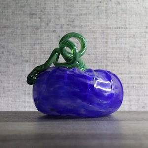May include: A blue and white glass pumpkin with a green glass stem. The pumpkin has a swirled design.