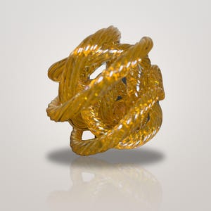 May include: A spherical sculpture crafted from translucent amber-colored glass, featuring a series of interconnected, twisted rope-like strands that create an intricate, open-work design with a reflective, glossy surface finish.