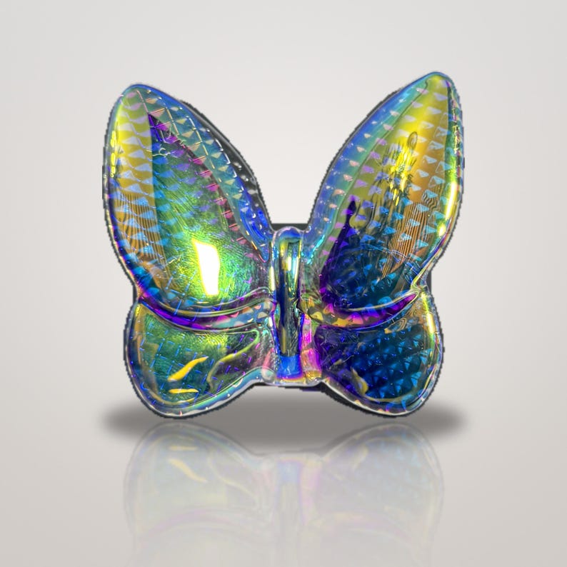 K&ouml;nnte beinhalten: Ein schmetterlingsf&ouml;rmiges Objekt mit einer stark reflektierenden, irisierenden Oberfl&auml;che, die zwischen Blau-, Gr&uuml;n- und Goldt&ouml;nen wechselt. Die Fl&uuml;gel weisen ein strukturiertes, geometrisches Muster auf, das das Licht einf&auml;ngt.