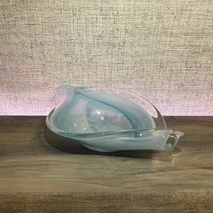 May include: A decorative glass bowl featuring a swirling pattern of translucent light blue and opaque white colors. The bowl has an elongated, asymmetrical leaf-like shape with curved, undulating edges that taper to pointed ends on both sides.