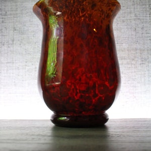 Può includere: Un vaso di vetro rosso e marrone con un motivo screziato. Il vaso ha un'ampia apertura e una base arrotondata.