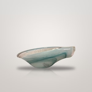 May include: A shallow, asymmetrical glass bowl featuring swirling patterns of translucent light blue and white. The bowl has a smooth, polished finish and includes a small black sticker on the side with the text MURANO.