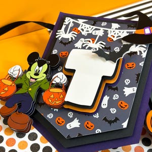 May include: A Halloween-themed banner with a Mickey Mouse character holding a pumpkin bucket. The banner features a black and white spider web design with bats, ghosts, and pumpkins. The banner is layered with different colors of cardstock, including purple, black, and orange.