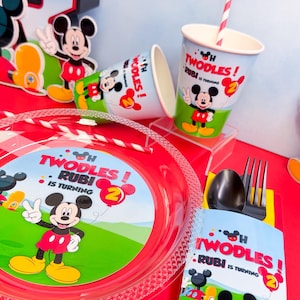 May include: Party supplies featuring Mickey Mouse. Includes plates, cups, and a utensil holder with the text "Twodles! Rubi is turning 2". The color scheme is red, white, yellow, and black.