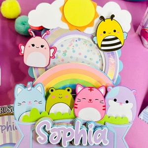 May include: A purple banner with the name 'Sophia' in white and purple letters. The banner is decorated with a rainbow, a cloud, a sun, a bee, a butterfly, a cat, a frog, and a hamster. The characters are all cartoon-like and have friendly faces.