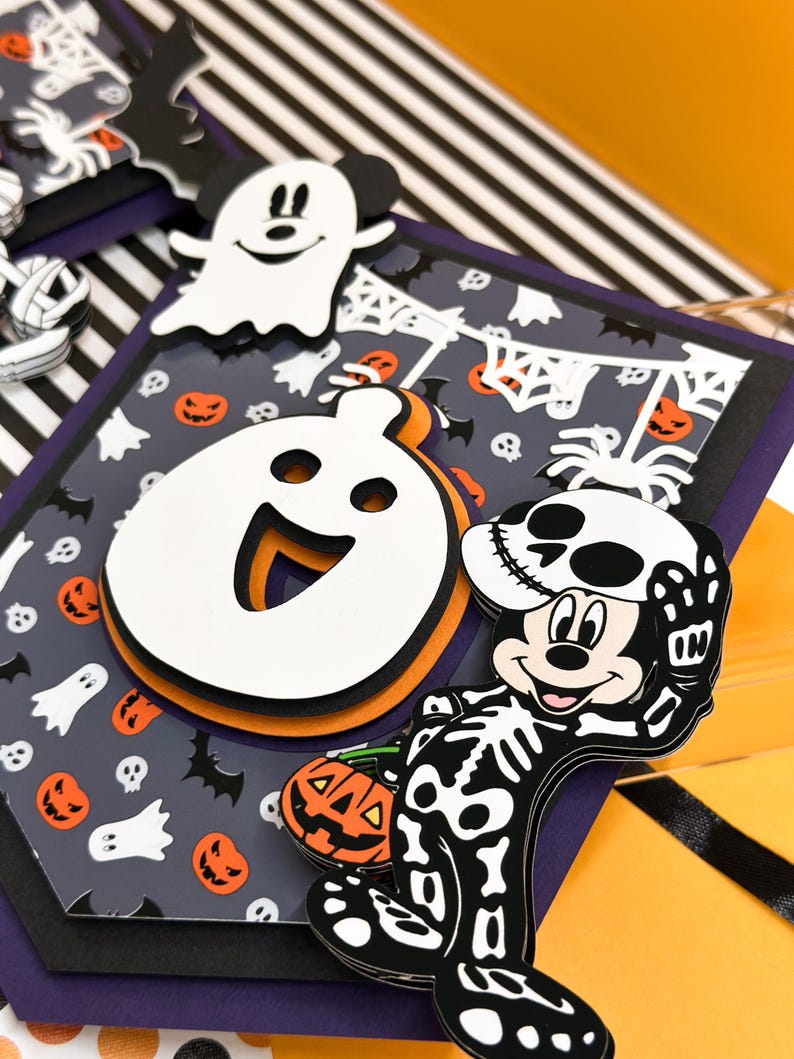 May include: A Halloween-themed banner with a black and white striped background. The banner features a Mickey Mouse character dressed as a skeleton holding a jack-o-lantern. The banner also features a ghost and a spider.